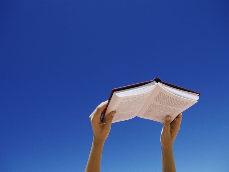 young-woman-holding-book-up-in-air-low-angle-view-royalty-free-image-1591044360.jpg