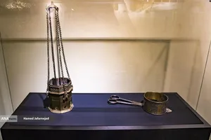 اسپنددودکن از جنس برنج دارای کتیبه وقف نامه و گُل گیر شمع مشبک و طلاکوب در اواخر دوره صفوی - نمایشگاه آثار منتخب گنجینه آستان قدس رضوی