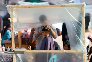 پسر آواره فلسطینی حین کوتاه کردن مو در اردوگاه رفح در جنوب نوار غزه